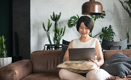 A smiling woman sitting on a couch using a laptop